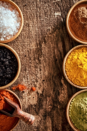 Border of colourful spice, Himalayan salt and black lava salt in bowls on either side of a wooden...