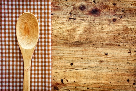 Wooden kitchen spoon on a fresh checkered rustic red and white napkin on a wooden counter with copyspaceの写真素材