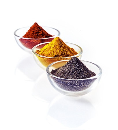 Three clear glass bowls of colourful of ground spice and black lava salt in conical heaps arranged...