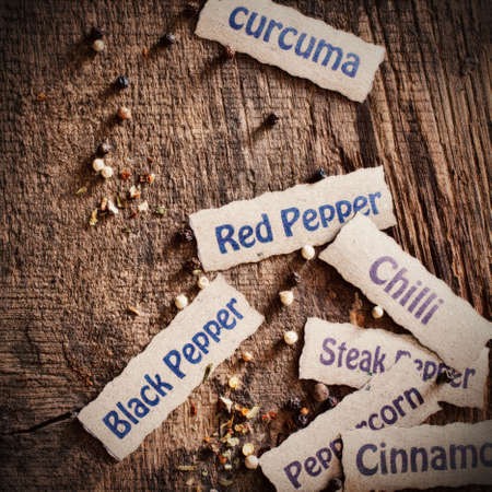 Scattered decorative name labels for spices with black and white peppercorns on a textured weathered...