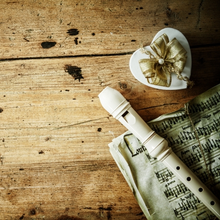 Conceptual image of Christmas night music with a recorder of flute lying on an old music score alongside a decorative heart shaped gift with an ornamental bow, copyspace on the rustic wood backgroundの写真素材