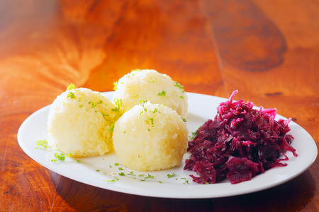 Three cooked potato balls and sauerkraut made from fermented red cabbage served on a side plate as an accompaniment to a mealの写真素材