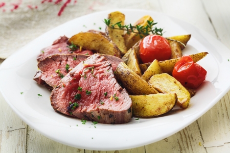 Delicious succulent rare beef steak sliced and served with roast potato wedges and tomato garnished with chopped parsleyの写真素材