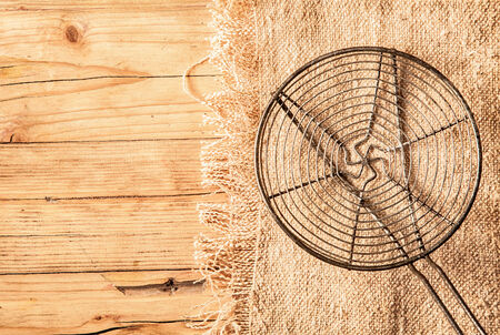 Circular metal grid or rack for baking and cooling freshly baked cakes in a country kitchen lying on a piece of hessian on an old wooden table top with copyspaceの写真素材