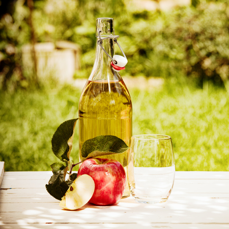 Bottled fresh apple juice served in the garden with a juicy red apple and glass under the shade of a treeの写真素材