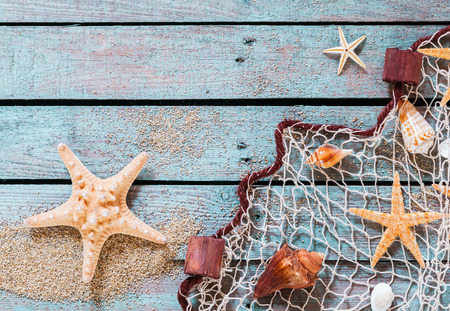 Marine still life on rustic wooden boards with scattered golden beach sand with a spiny starfish and fishing net covered in carefully arranged shells and sea stars with copyspaceの写真素材