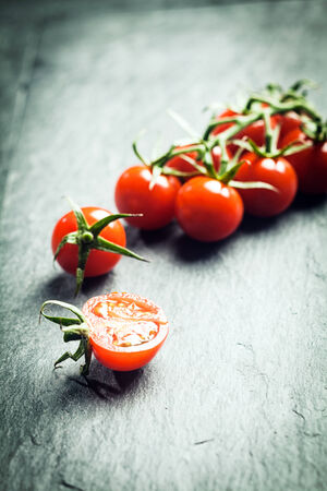 Grape tomatoes on the vine with a single halved tomato in the foreground on a textured surface with highlight and copyspace and shallow dofの写真素材