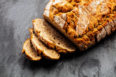 Freshly baked sliced loaf of crusty rye bread viewed from above over a dark background showing the...