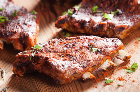 Close up of a portion of barbecued grilled ribs seasoned with hot spices and fresh herbs on a wooden boardの写真素材