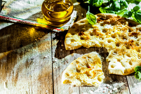 Focaccia bread, a traditional Italian flatbread flavored with olive oil and salt and topped with herbs served on rustic weathered wooden boards in a country kitchen with fresh basilの写真素材