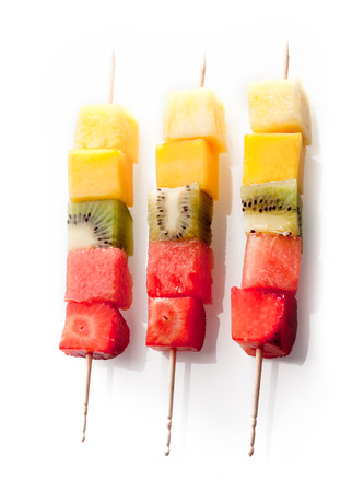 Trio of colorful, healthy fresh fruit kebabs with neatly cut cubes of exotic and tropical fruits arranged in a row on a white backgroundの写真素材