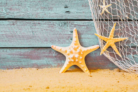 Nautical background with starfish and a fishing net against rustic weathered blue wooden planks above golden beach sandの写真素材