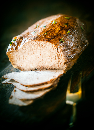 Sliced German meat loaf cooked in a casserole and garnished with fresh chopped herbs on a dark background with a carving forkの写真素材