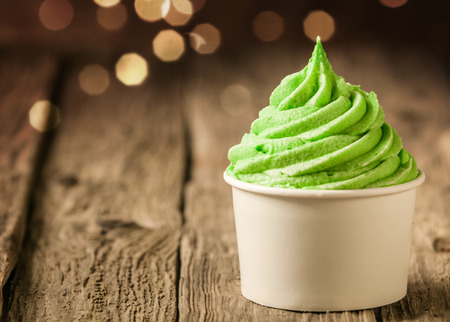Tub of twirling creamy green Italian ice cream on a rustic wood table with a sparkling bokeh of party lightsの写真素材