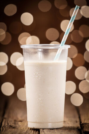 Creamy fruity smoothie on an old wooden bar counter against a festive brown bokeh of sparkling party lights at a summer celebrationの写真素材
