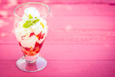 Chilled strawberry pavlova or parfait in a tall glass with farm fresh strawberries, cream, meringue and ice cream for a gourmet summeer dessert, pink wood background with copyspaceの写真素材