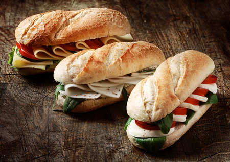 Freshly baked crusty golden vegetarian baguettes in a bakery with a variety of cheese, herb and salad fillings on a rustic wood background, closeup viewの写真素材