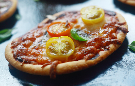 Italian mini pizza with cheese and tomato on a thick golden crusty base topped with fresh basil, close up viewの写真素材