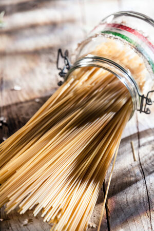 Healthy wholewheat Italian spaghetti pasta in a glass jar with the colors of the Italian national flag lying on its side on a rustic wooden surface in sunshineの写真素材