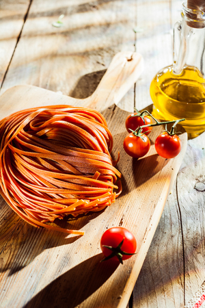 Ingredients for a tasty Italian tomato pasta dish with flavored linguine pasta. cherry tomatoes and olive oil on a chopping board on a rustoc wooden kitchen tableの写真素材