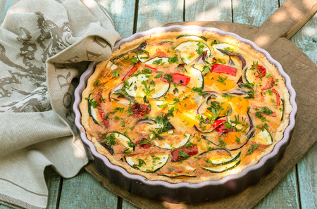 Delicious eggplant savory tart with tomato and fresh herbs in a fluted pie dish served on a wooden board outdoors for a summer picnicの写真素材