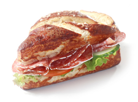 Delicious crusty brown lye bread roll sandwich, a traditional German and Bavarian bread glazed with lye, with spicy salami sausage, lettuce, cucumber and tomato on whiteの写真素材