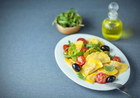 Ravioli, olive, arugula and tomato Italian salad served with fresh virgin olive oil and a side dish of fresh rocket on a grey cloth with copyspaceの写真素材