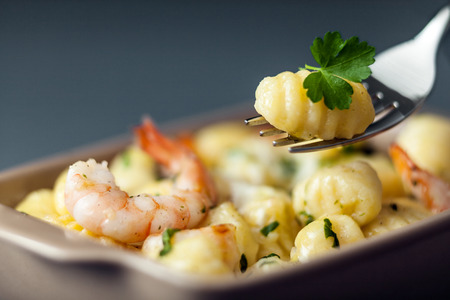 Italian gnocchi pasta, or dumplings made with semolina, with prawns or shrimps for a delicious seafood cuisine with one dumpling on a fork with selective focusの写真素材