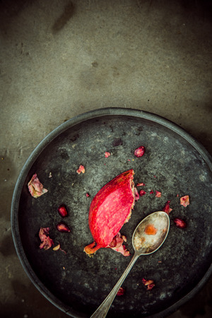 Partial remnants of a fresh pomegranate on a rustic plate with a spoon used to remove and eat the juicy ripe red seeds, overhead view with copyspaceの写真素材
