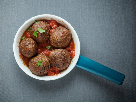 Tasty seasoned meatballs in a saucepan with a hot spicy chili pepper and tomato sauce and fresh herbs, overhead viewの写真素材