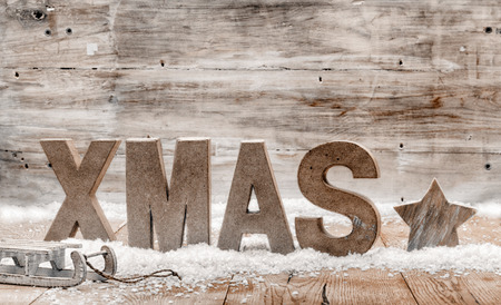 Wood craft rustic Christmas background with wooden letters spelling Xmas standing in snow with a star and small kids sleigh or toboggan against a weathered wooden wall with copyspace for your greetingの写真素材