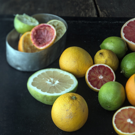 Juicing a selection of fresh citrus fruit with grapefruit, oranges, limes and lemons and a metal container with squeezed skin remnantsの写真素材