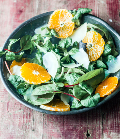 Bowl of fresh green leafy marche, sliced orange and parmesan cheese salad on a vintage wooden background, high angle viewの写真素材