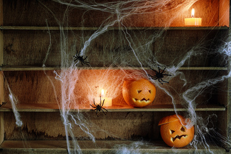 Two Halloween Jack o Lanterns Carved from Oranges and Spiderwebs with Spiders and Lit Candles on Shelvesの写真素材