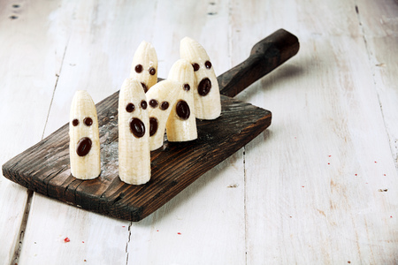 Banana Halloween Ghosts with Chocolate Faces on Wooden Cutting Boardの写真素材
