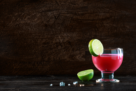 Healthy fruit cocktail made with mixed berries blended with alcohol garnished with a slice of fresh lime standing on a bar counter against a dark background with copyspaceの写真素材