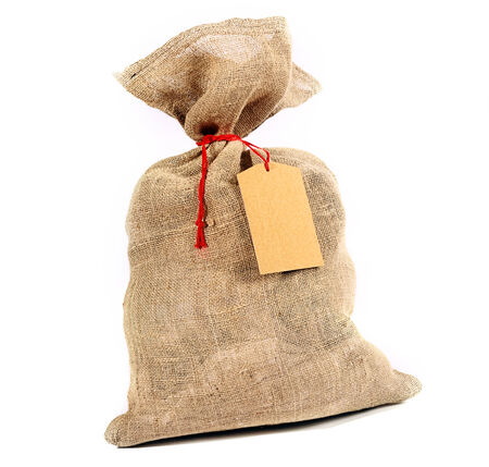 Rustic burlap sack tied with red string with a blank gift tag for your Christmas or seasonal greeting over whiteの写真素材