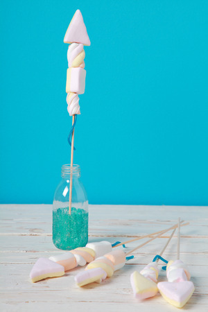 Homemade edible fireworks party favors in the shape of rockets made from colorful marshmallows, on a rustic wooden table against a blue background with copyspaceの写真素材