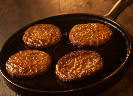 Four cooked spicy beef patties or frikadeller in a metal frying pan or skillet ready to be used to make burgersの写真素材