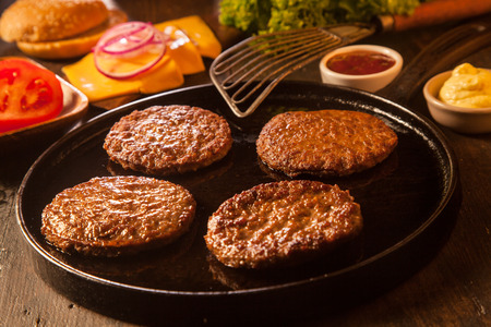 Preparing a batch of cheeseburgers with assorted ingredients and four grilled ground beef patties or frikadeller in a panの写真素材