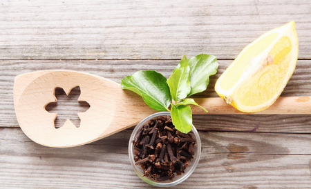 Overhead view of a decorative wooden spoon with a flower pattern cut out alongside a dish of dried aromatic cloves and a wedge of lemon on grey wooden rustic boardsの写真素材