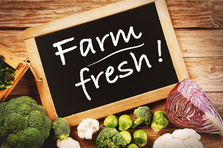 Black Chalk Board with Farm Fresh Texts with Assorted Organic Veggies on Sides on Top of Wooden Table.の写真素材