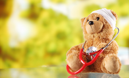 Close up Bandaged Plush Teddy Bear with Stethoscope Device on Top of a Glass Table, Emphasizing Copy Space.の写真素材