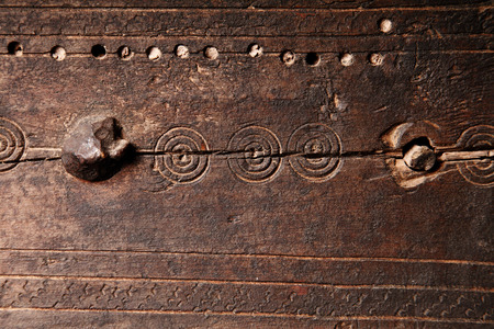 Old medieval style wooden background texture with a weathered cracked panel of wood with iron studs,...