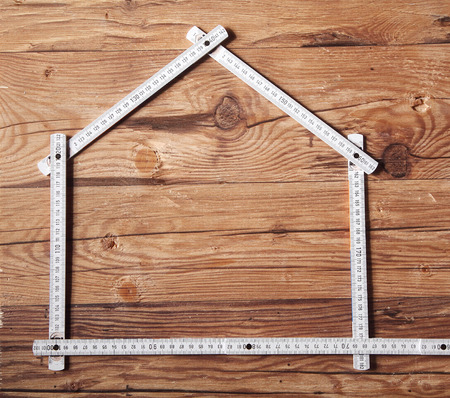 Conceptual White Folding Ruler Forming a House on Top of a Brown Wooden Tableの写真素材