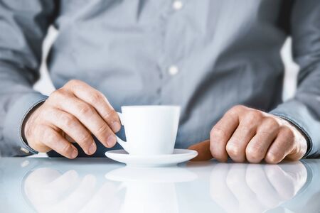 Businessman enjoying a coffee break sitting at his desk drinking a cup of hot beverage, close up...