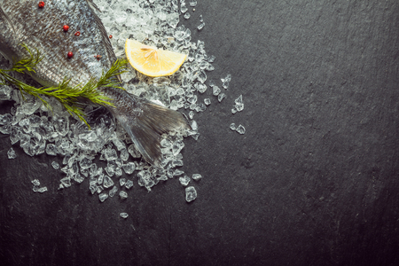 Fresh fish on crushed ice with dill displayed with the tail visible in the top left corner of the frame on a slate background with copyspaceの写真素材