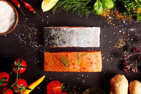 Overhead view of a frame of fresh ingredient including herbs, spices, root ginger, tomato, and chili pepper with raw salmon steaks for a gourmet recipe for a seafood dinnerの写真素材