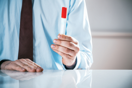 Businessman sitting at a table in the office in a meeting gesturing with a marker pen to emphasise a point or draw attention, close up of his handsの写真素材