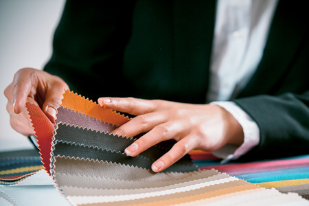 Close up view of the hand of a woman checking fabric color swatches for interior decorating on a counter topの写真素材